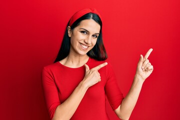 Young hispanic woman wearing casual clothes smiling and looking at the camera pointing with two hands and fingers to the side.