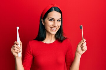 Young hispanic woman choosing electric toothbrush or normal teethbrush smiling with a happy and...