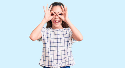 Cute hispanic child girl wearing casual clothes doing ok gesture like binoculars sticking tongue out, eyes looking through fingers. crazy expression.