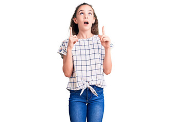 Cute hispanic child girl wearing casual clothes amazed and surprised looking up and pointing with fingers and raised arms.