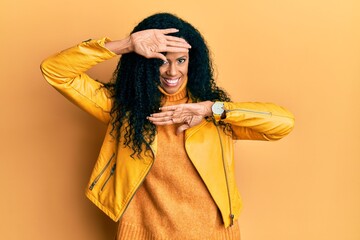 Middle age african american woman wearing wool winter sweater and leather jacket smiling cheerful playing peek a boo with hands showing face. surprised and exited