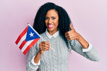 Middle age african american woman holding puerto rico flag smiling happy and positive, thumb up doing excellent and approval sign