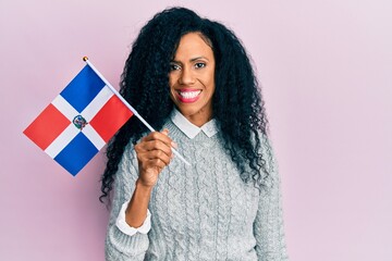 Middle age african american woman holding dominican republic flag looking positive and happy...