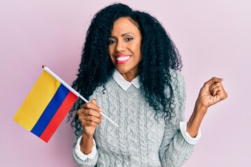 Middle age african american woman holding colombia flag screaming proud, celebrating victory and success very excited with raised arm