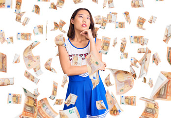 Young beautiful chinese girl wearing cheerleader uniform with hand on chin thinking about question,...