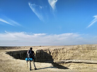 Man with a backpack looking at a crater in the desert of Turkmenistan