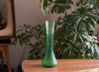 Mid century modern green glass vase on a wooden table - in the background plants