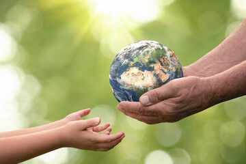 Close up of senior hands giving small planet earth to a child over defocused green background with copy space - 409608980