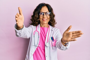 Middle age hispanic woman wearing doctor uniform and glasses looking at the camera smiling with open arms for hug. cheerful expression embracing happiness.