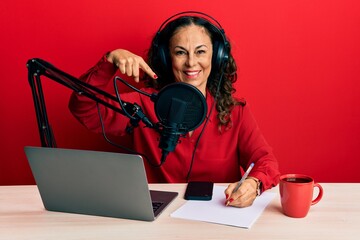 Beautiful middle age woman working at radio studio smiling happy pointing with hand and finger