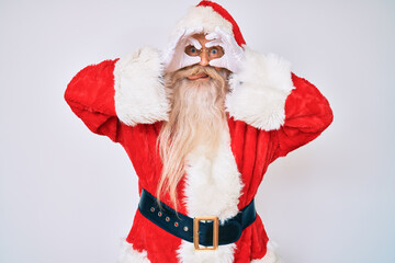 Old senior man with grey hair and long beard wearing santa claus costume with suspenders doing ok gesture like binoculars sticking tongue out, eyes looking through fingers. crazy expression.
