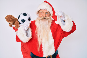 Old senior man with grey hair and long beard wearing santa claus costume holding mustache smiling and laughing hard out loud because funny crazy joke.