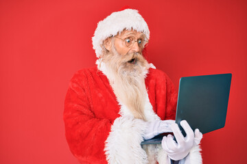Old senior man with grey hair and long beard wearing santa claus costume using laptop celebrating crazy and amazed for success with open eyes screaming excited. - Powered by Adobe