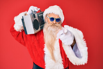 Old senior man wearing santa claus costume and boombox pointing with finger to the camera and to you, confident gesture looking serious