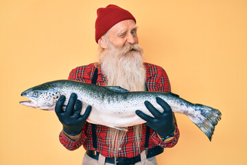 Old senior man with grey hair and long beard showing raw salmon winking looking at the camera with...