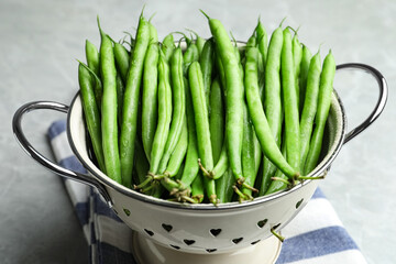 Fresh green beans in colander on light table, closeup