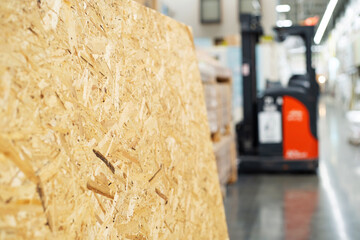 OSB panel in a building materials store. A fragment of a board made of shavings and glue against the background of a self-propelled loader and a sales area. Foreground. Selective focus