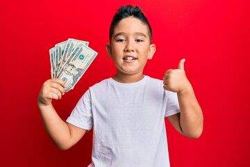Little boy hispanic kid holding 20 dollars banknotes smiling happy and positive, thumb up doing...