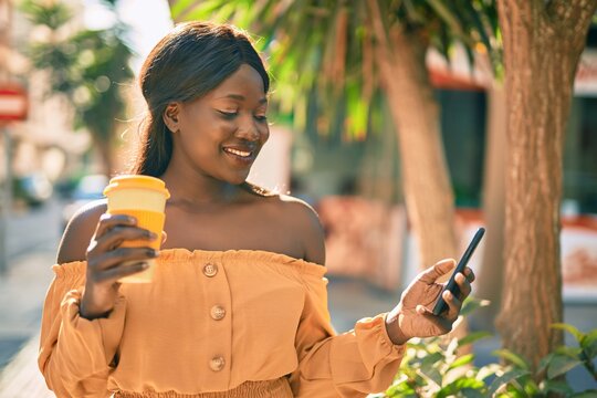 Young african american woman using smartphone drinking coffee at the city.