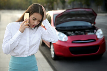 Stressed woman talking on phone near broken car outdoors