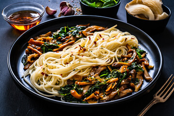 Asian food - fried soy sauce oyster mushrooms with noodles on black stone

