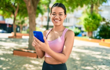 Young beautiful hispanic sporty woman wearing fitness outfit smiling happy and natural texting using smartphone at the town