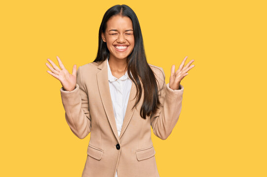 Beautiful hispanic woman wearing business jacket celebrating mad and crazy for success with arms raised and closed eyes screaming excited. winner concept