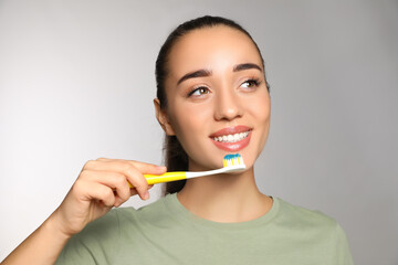 Woman holding toothbrush with paste on light background