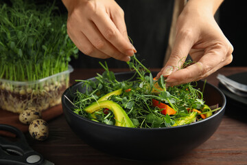 Woman making salad with fresh organic microgreen at wooden table, closeup