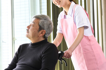  車椅子に乗ったシニア男性と若いエプロン姿の介護士の女性