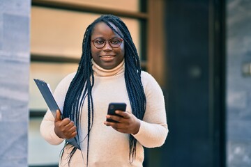 Young african american woman using smartphone and holding clipboard at the city.