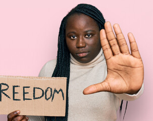 Young black woman with braids holding freedom banner with open hand doing stop sign with serious...