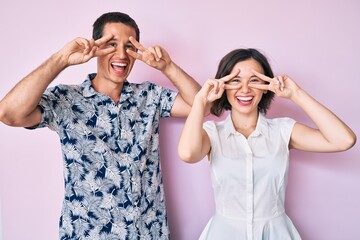 Beautiful couple wearing casual clothes doing peace symbol with fingers over face, smiling cheerful showing victory