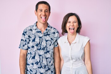 Beautiful couple wearing casual clothes sticking tongue out happy with funny expression. emotion concept.