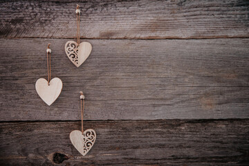 Valentine's Day background. Brown natural boards in grunge style with three wooden decorative hearts. Top view. Surface of table to shoot flatlay. Concept love, romantic relation. Copy space for text.