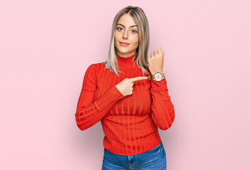 Beautiful blonde woman wearing casual clothes in hurry pointing to watch time, impatience, looking...