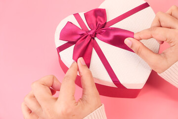 women hand holding a heart shape gift box on pink 