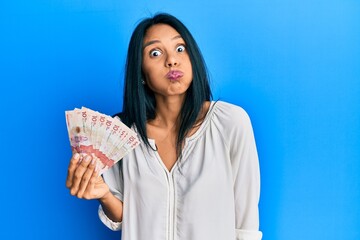 Young african american woman holding 10 colombian pesos banknotes puffing cheeks with funny face. mouth inflated with air, crazy expression.