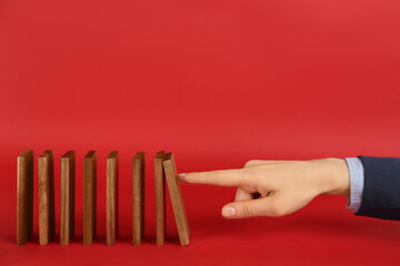 Woman causing chain reaction by pushing domino tile on red background, closeup. Space for text