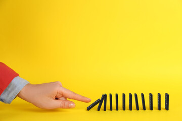Woman causing chain reaction by pushing domino tile on yellow background, closeup. Space for text