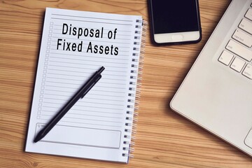 Disposal of fixed assets label on notepad with laptop and smartphone