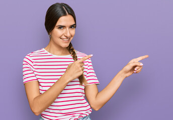 Young hispanic woman wearing casual clothes smiling and looking at the camera pointing with two hands and fingers to the side.