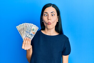 Beautiful young woman holding dollars making fish face with lips, crazy and comical gesture. funny expression.