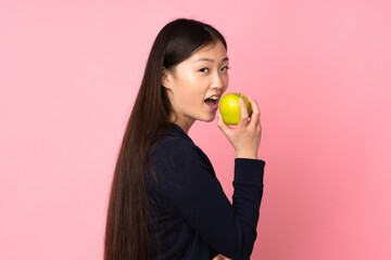 Young asian woman isolated on pink background eating an apple