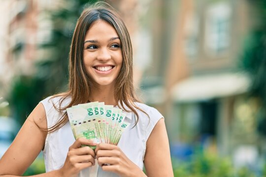 Beautiful latin teenager girl smiling happy holding hong kong dollars at the city.