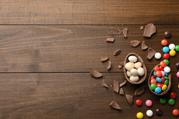 Obraz na płótnie Canvas Broken chocolate egg and colorful candies on wooden table, flat lay. Space for text