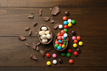 Broken chocolate egg and colorful candies on wooden table, flat lay