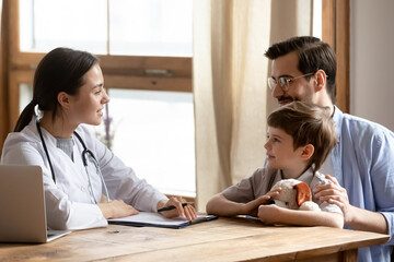 Caring female pediatrician talk consult little boy patient at consultation in private clinic with dad. Woman GP doctor consult small child visit do checkup with father in hospital. Healthcare concept.