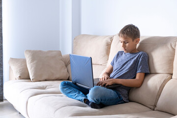 Boy doing homework task with laptop computer, watching video at home. Technology, education, online remote learning for kids. Stay at home entertainment