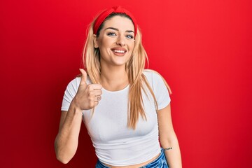 Young caucasian woman wearing casual white t shirt doing happy thumbs up gesture with hand. approving expression looking at the camera showing success.